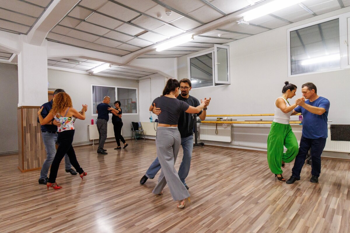 Cupluri exersând tango argentinian, în sala de curs